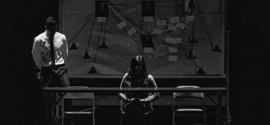 Dark room with an investigator standing behind suspect