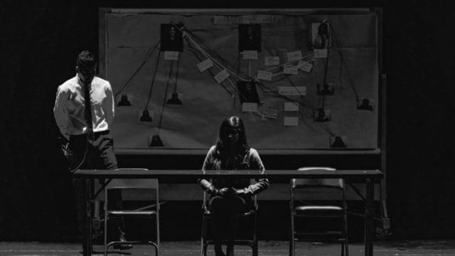 Dark room with an investigator standing behind suspect