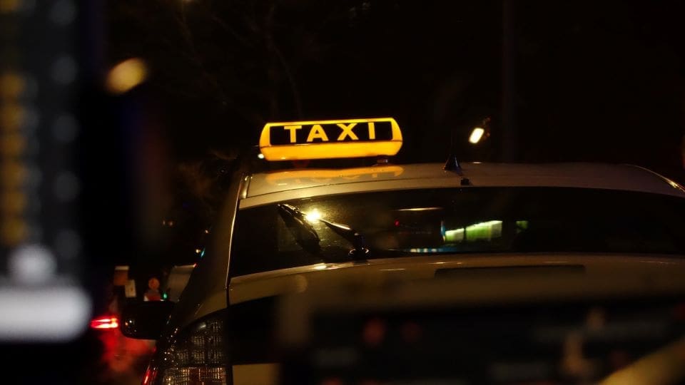 A white car with a yellow sign reading "Taxi" on the top