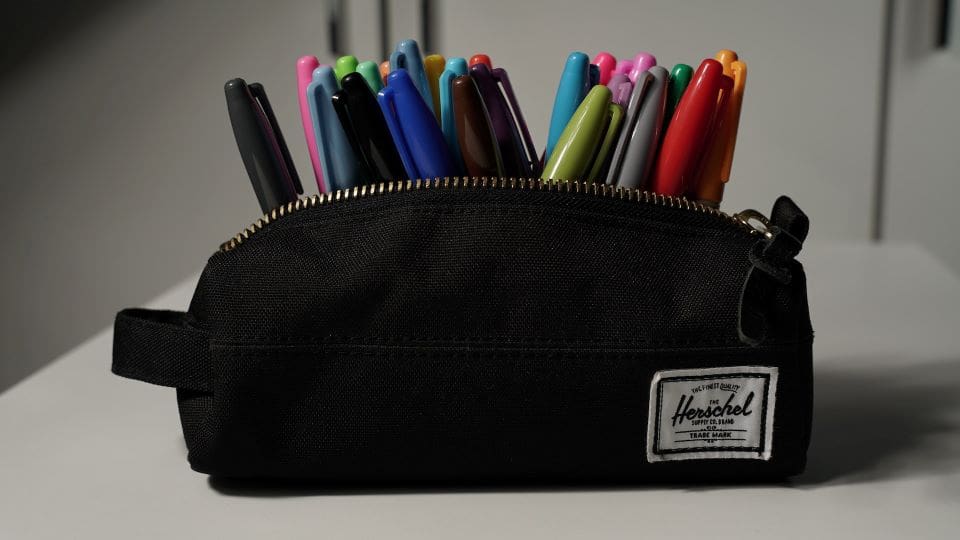 Bag of Sharpie Markers | CaseGuard Black pencil bag, unzipped, filled with different colored sharpie markers sitting on a white table.