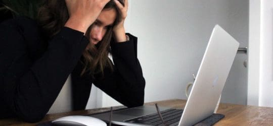 Brunette woman with her hands on her head in frustration looking at an open laptop.