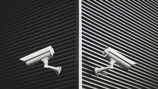 Two security cameras facing opposite directions on the corner of a building.