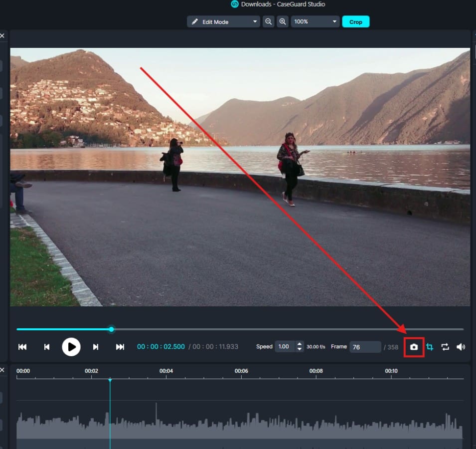 Video editing interface showing a lakeside scene with mountains and two people; a red diagonal crop guide highlights the crop tool at the bottom right.