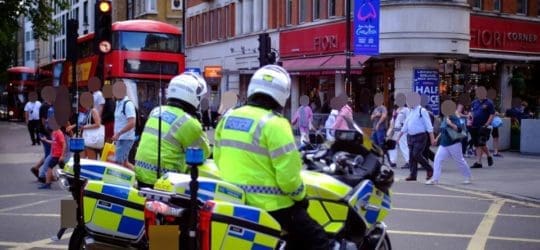 Two police officers on motor cycles watching people use a cross walk in the UK.